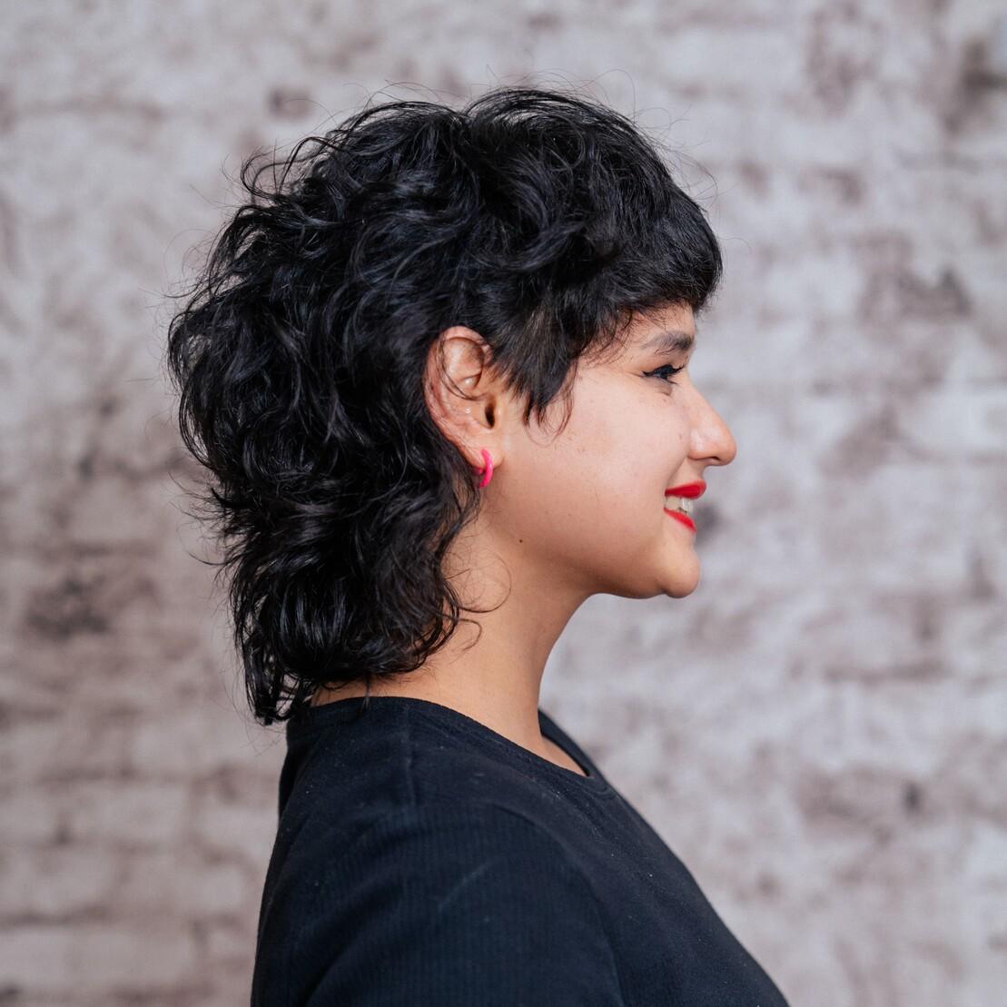 Profilansicht einer Person mit kurzem, lockigem Mullet. Die gestufte Form und definierte Locken sind deutlich sichtbar.